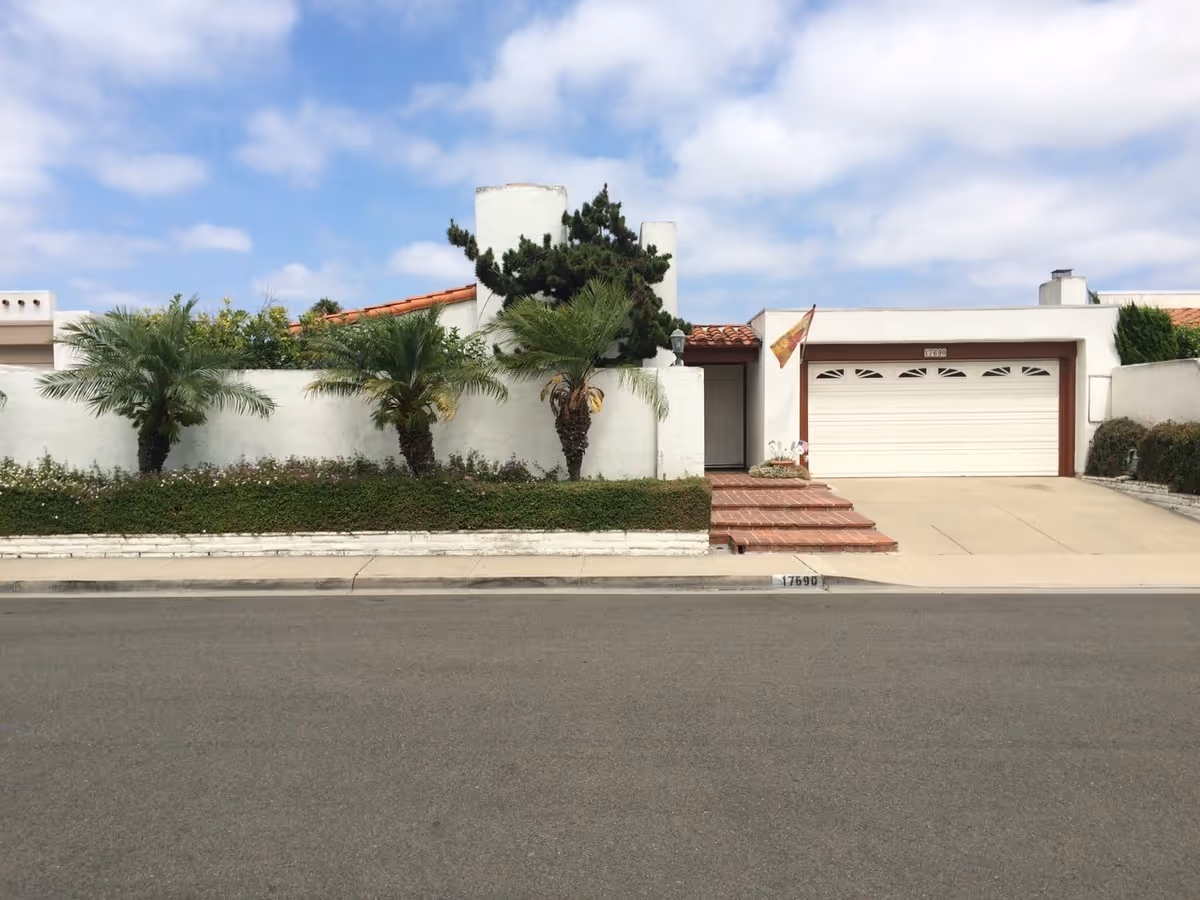 Exterior view of a white residential building with a garage and palm trees.