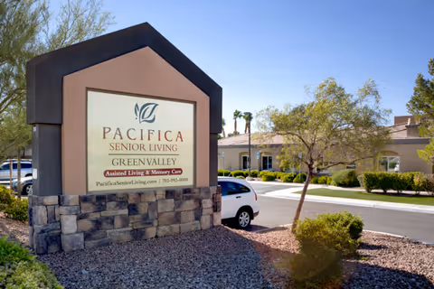 Outdoor view of the entrance sign for Pacifica Senior Living Green Valley, an assisted living and memory care facility, with a building and landscaping visible in the background under a clear blue sky.