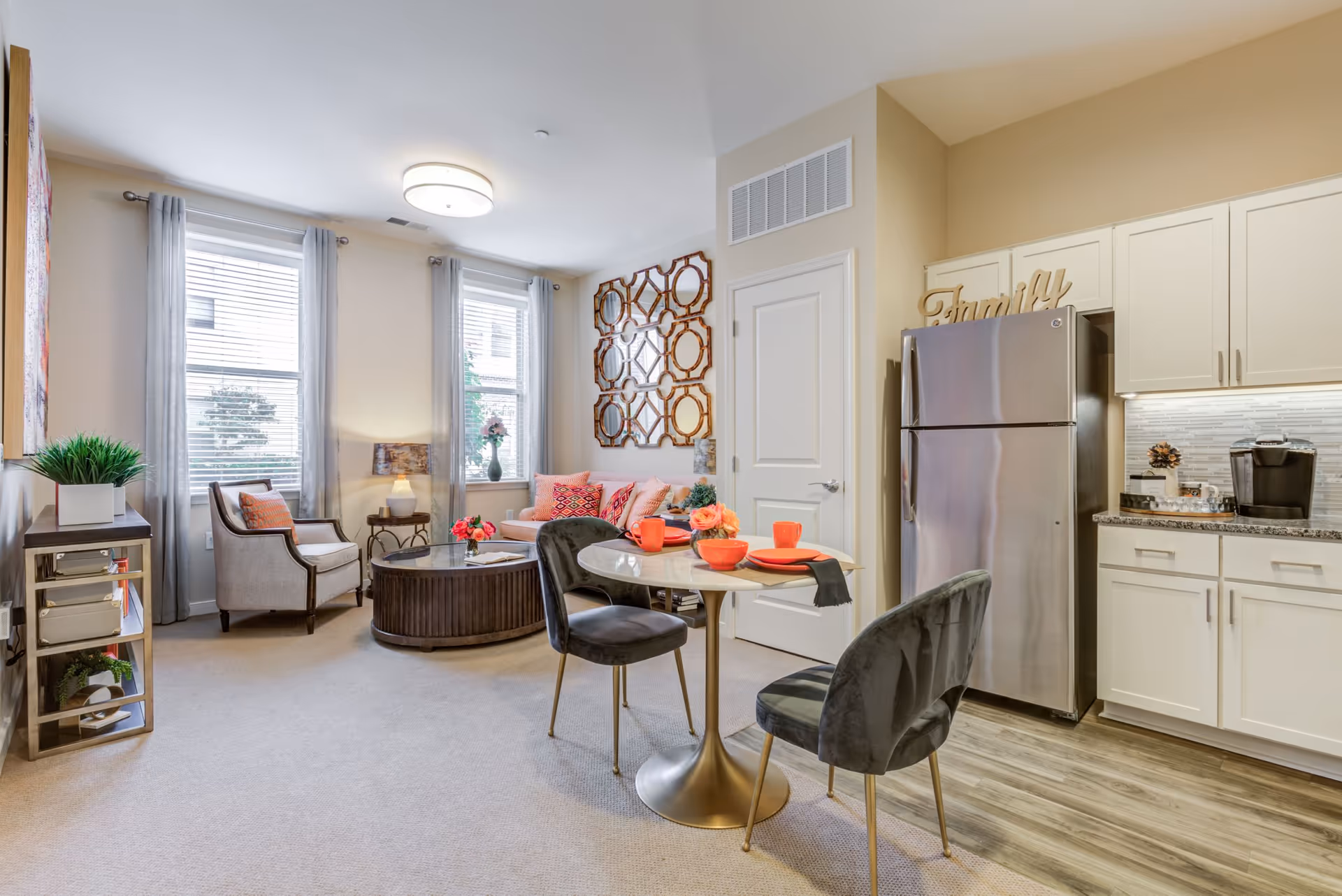 Open-concept living area with a small dining table, cozy seating and coffee table, and a kitchenette with a stainless steel refrigerator.