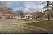 Low single-story building with a white portico and flagpole set behind a wide grassy lawn and scattered trees.