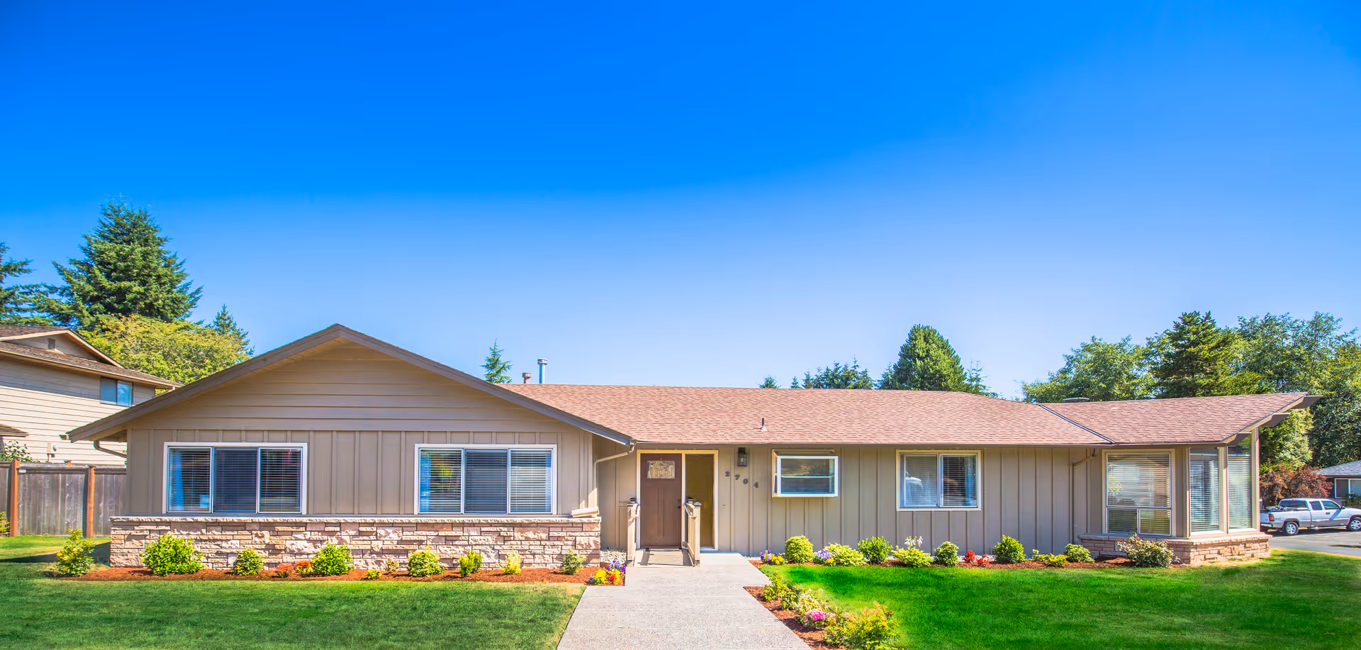 Front view of a single-story ranch-style home with a manicured green lawn under a clear blue sky.