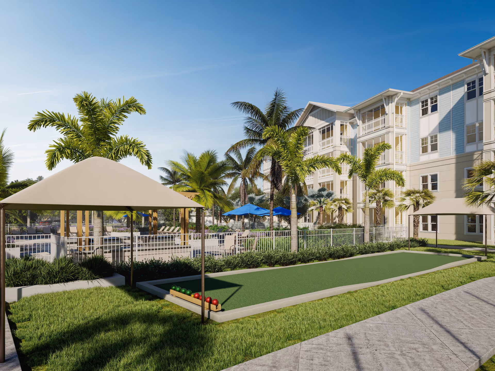 Outdoor area of The Sovana At Stuart featuring a bocce ball court with bocce balls lined up, shaded seating areas with beige canopies, palm trees, and a multi-story residential building in the background under a clear blue sky.