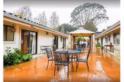 Outdoor courtyard with metal patio tables and chairs, a gazebo, and single-story buildings surrounding a wet paved area.