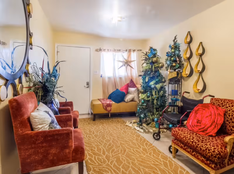 A decorated communal living room with upholstered chairs, a sofa, a Christmas tree and a walker.