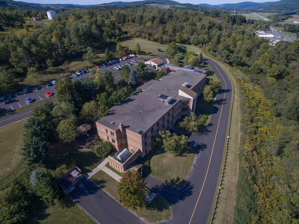 Aerial view of a brick rehabilitation and nursing center building surrounded by trees, parking lots, and a curving road.