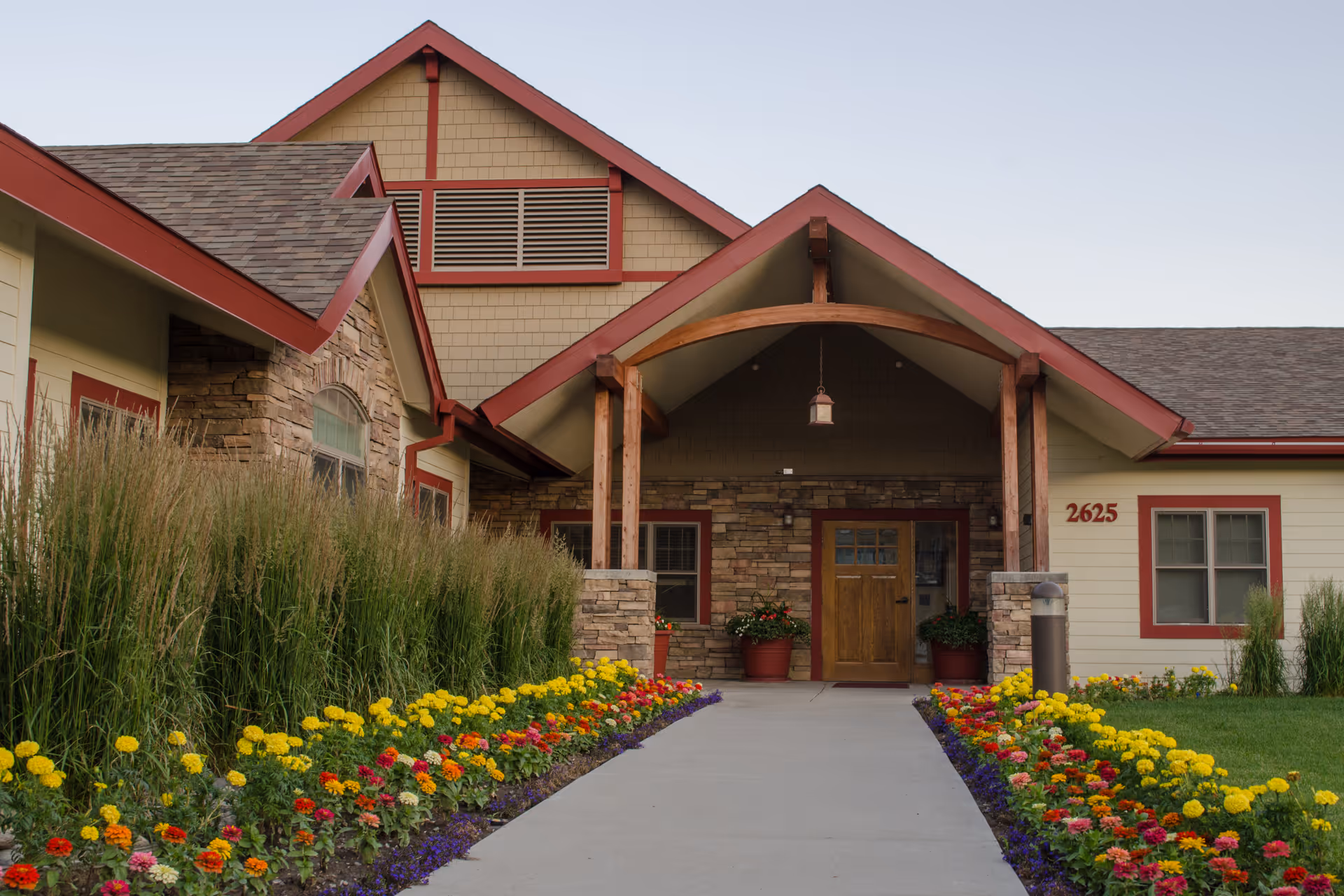 Entrance of a single-story building with a covered porch, wooden door, and a flower-lined walkway.