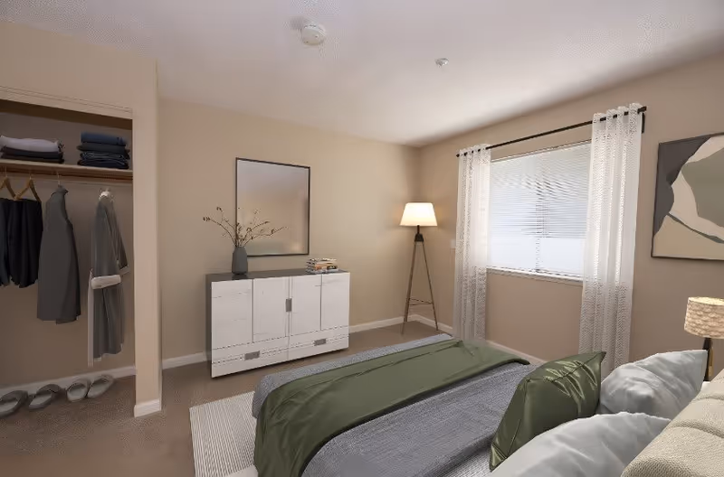 A bedroom with a bed covered in gray and green bedding, a white dresser with a vase and books on top, a floor lamp in the corner, a window with white curtains, an open closet with hanging clothes and shoes, and a piece of abstract wall art.