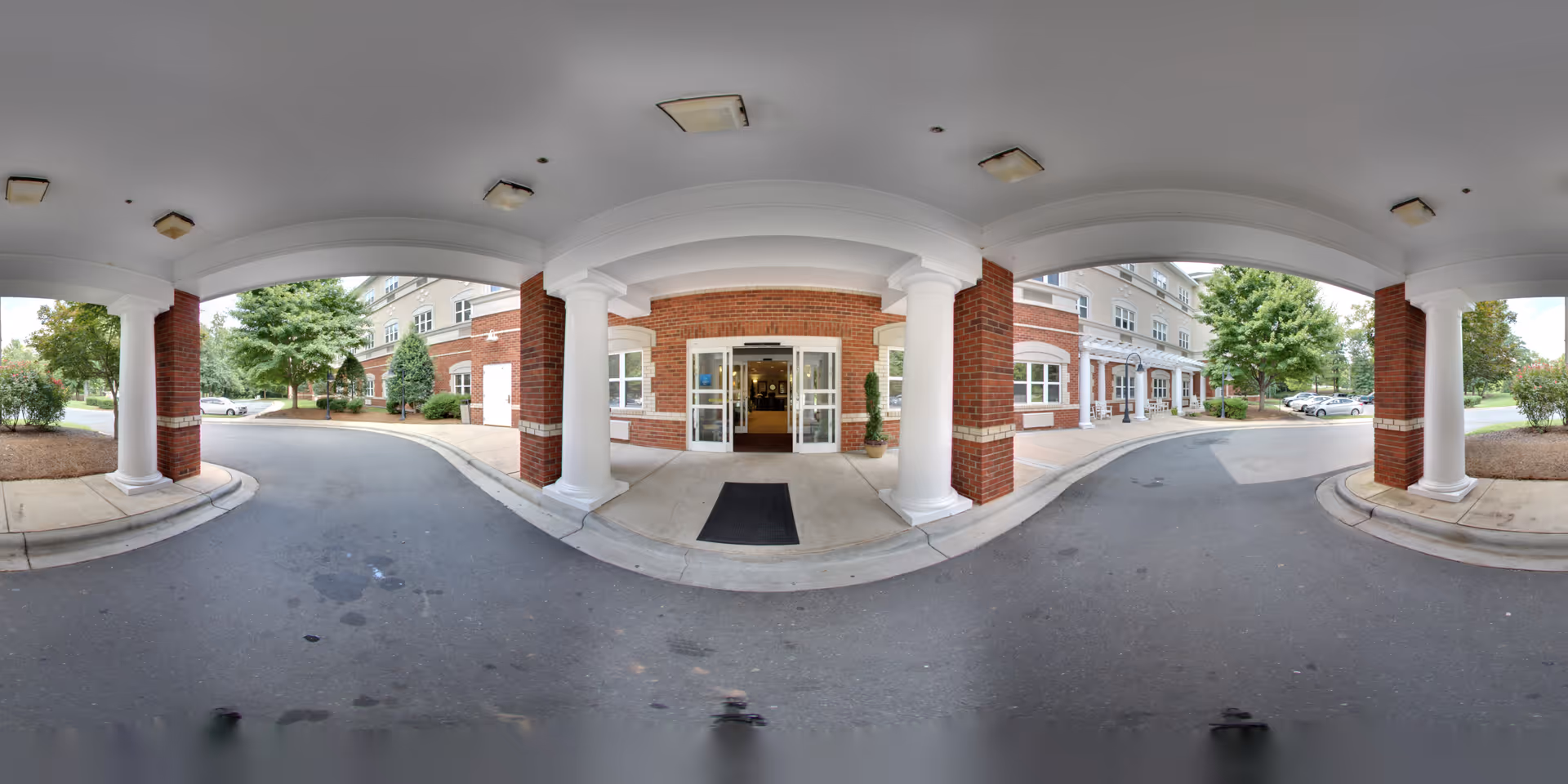 Covered porte-cochere entrance with white columns, a brick facade, and a circular driveway leading to glass double doors.