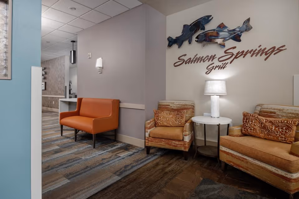 Seating area with orange chairs, a side table and lamp beneath a wall sign reading "Salmon Springs Grill".