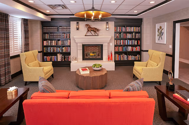 Comfortable communal living room with a central fireplace flanked by bookshelves, an orange sofa, two yellow armchairs, and a wooden coffee table.