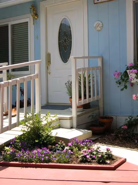 Blue house exterior with white door, railing, and potted flowers on porch.