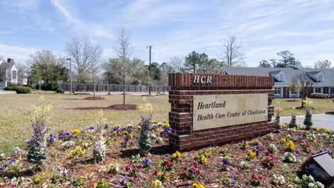 Brick sign for Heartland Health Care Center of Charleston with colorful flower beds in front.