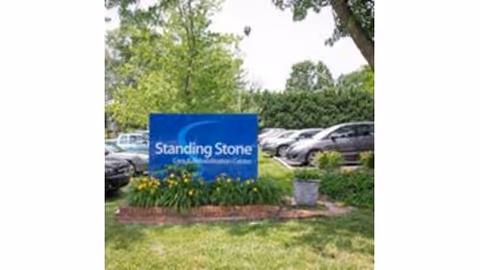 Blue Standing Stone sign in a landscaped lawn with parked cars and trees behind it.