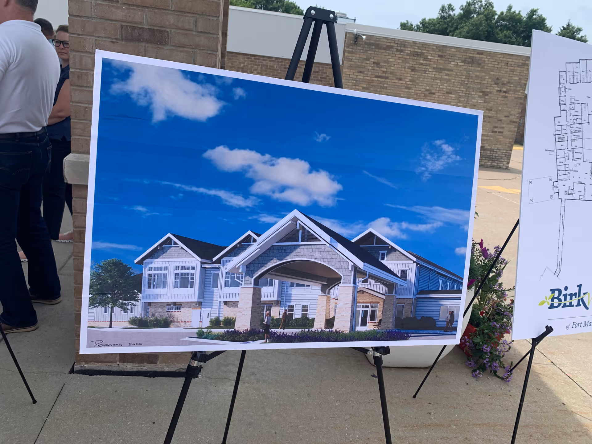 An architectural rendering of a white two-story building displayed on an easel outdoors.