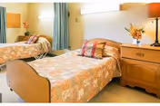 A bright bedroom with two twin beds, a wooden nightstand between them topped with a lamp and flowers, and curtains at the window.