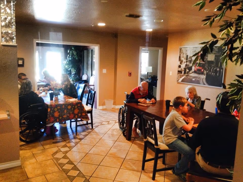 Seniors and guests sitting at tables and eating in a tiled dining room with wheelchairs and wall art.