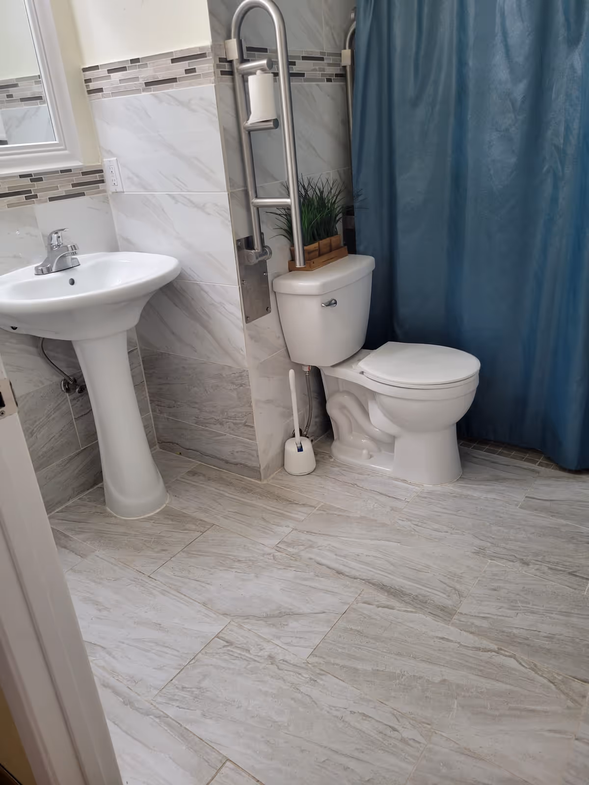 Small bathroom with a pedestal sink, toilet, stainless steel grab bar, and a blue shower curtain.