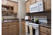 Compact kitchen with oak cabinets, white microwave and stove, sink, and dark countertops.