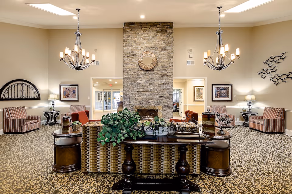 Spacious, well-lit communal lounge with seating arranged around a central table and a stone fireplace feature wall.