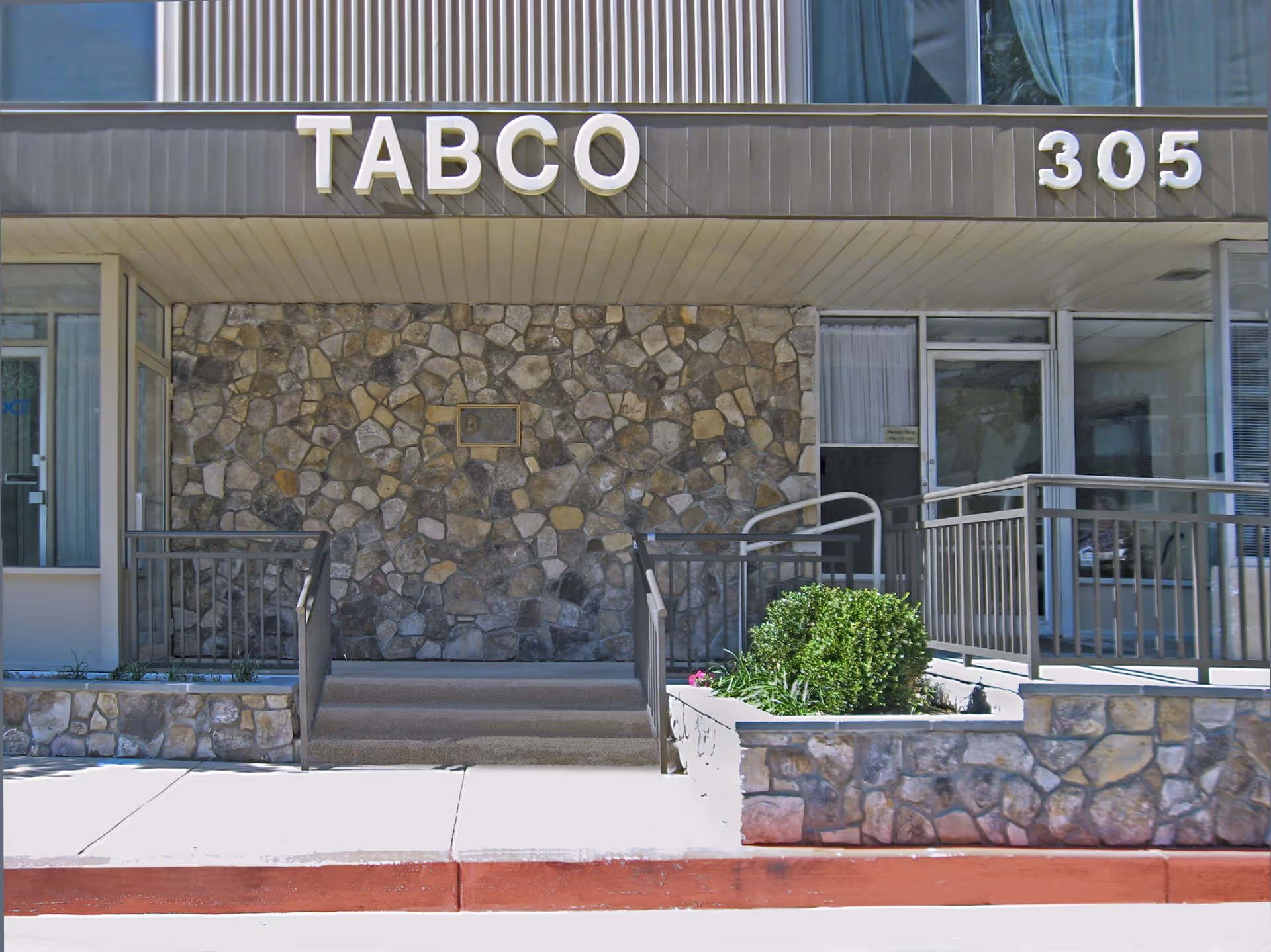 Entrance of Tabco Towers building with stone facade, stairs and a ramp leading to glass doors. The building number 305 is displayed on the right side above the entrance.