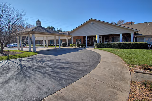 Exterior view of Brookdale Union senior living facility showing a single-story building with a covered entrance driveway, a gazebo structure to the left, and a curved sidewalk surrounded by grass and trees under a clear blue sky.