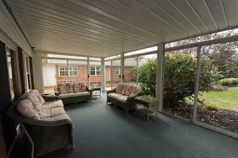 Enclosed sunroom lounge with wicker sofas and glass walls overlooking a garden.
