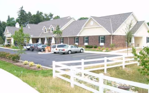 Exterior view of Bickford of Okemos front with parked cars and a white fence.