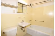 Small bathroom with yellow tiled walls featuring a bathtub with shower, toilet, wall-mounted sink, and mirrored medicine cabinet.