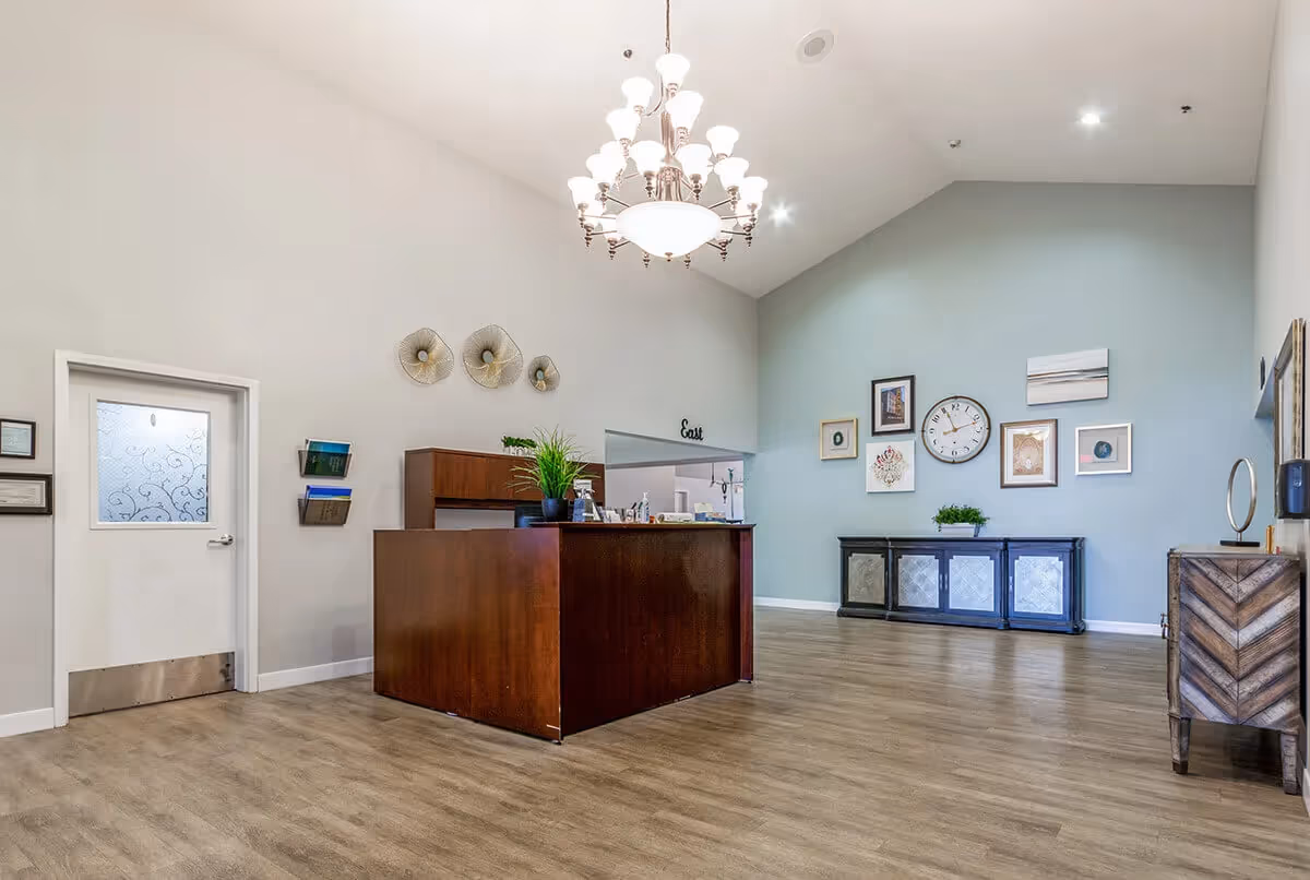 Spacious reception lobby with a wooden front desk, chandelier, decorative wall art, and a console against a pale blue wall.