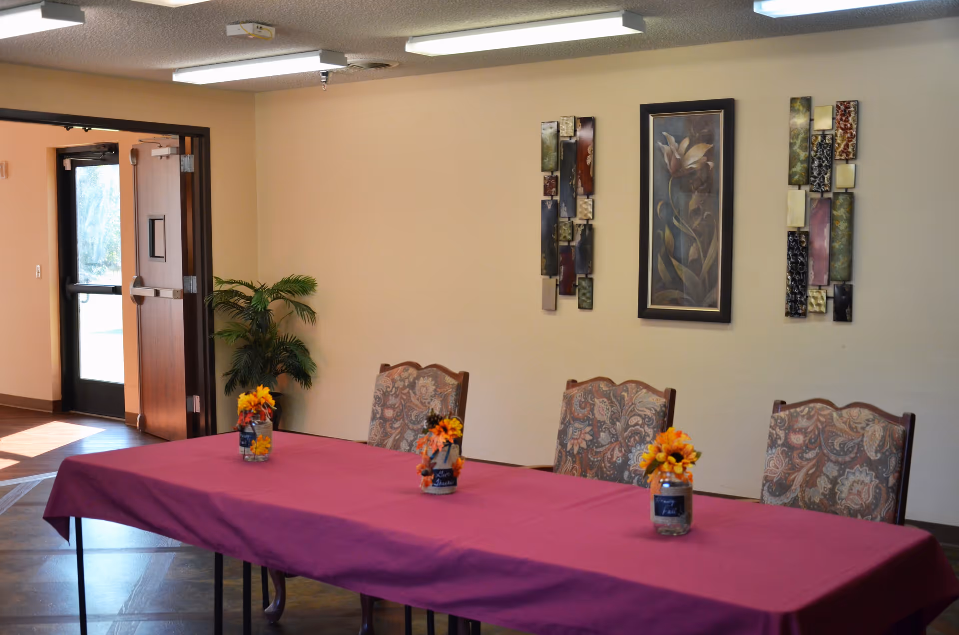A dining table covered with a purple tablecloth and small floral centerpieces in a room with upholstered chairs and wall art.