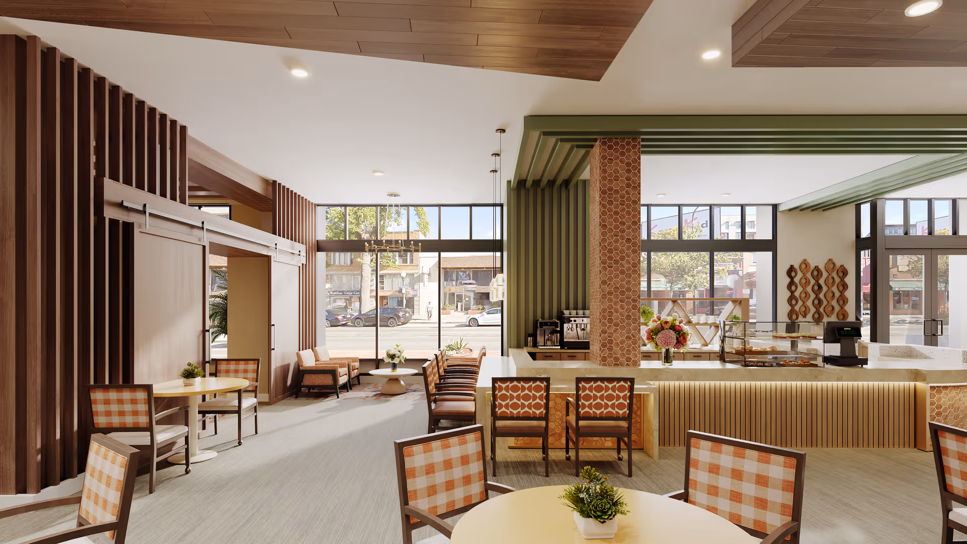 A bright and modern dining area with large windows letting in natural light. The space features several tables with orange and white checkered chairs, a counter with bar stools, and decorative wooden and green accents. Outside the windows, a street with parked cars and buildings is visible.