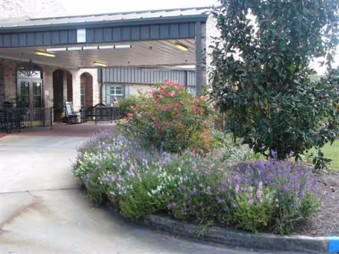 Covered entrance of Flannery Oaks Guest House with flowering shrubs and seating.