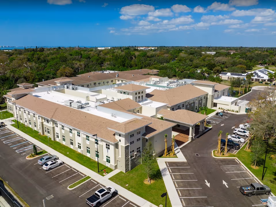 Aerial view of a large multi-wing senior living facility with parking lots, an entrance canopy, and surrounding trees.