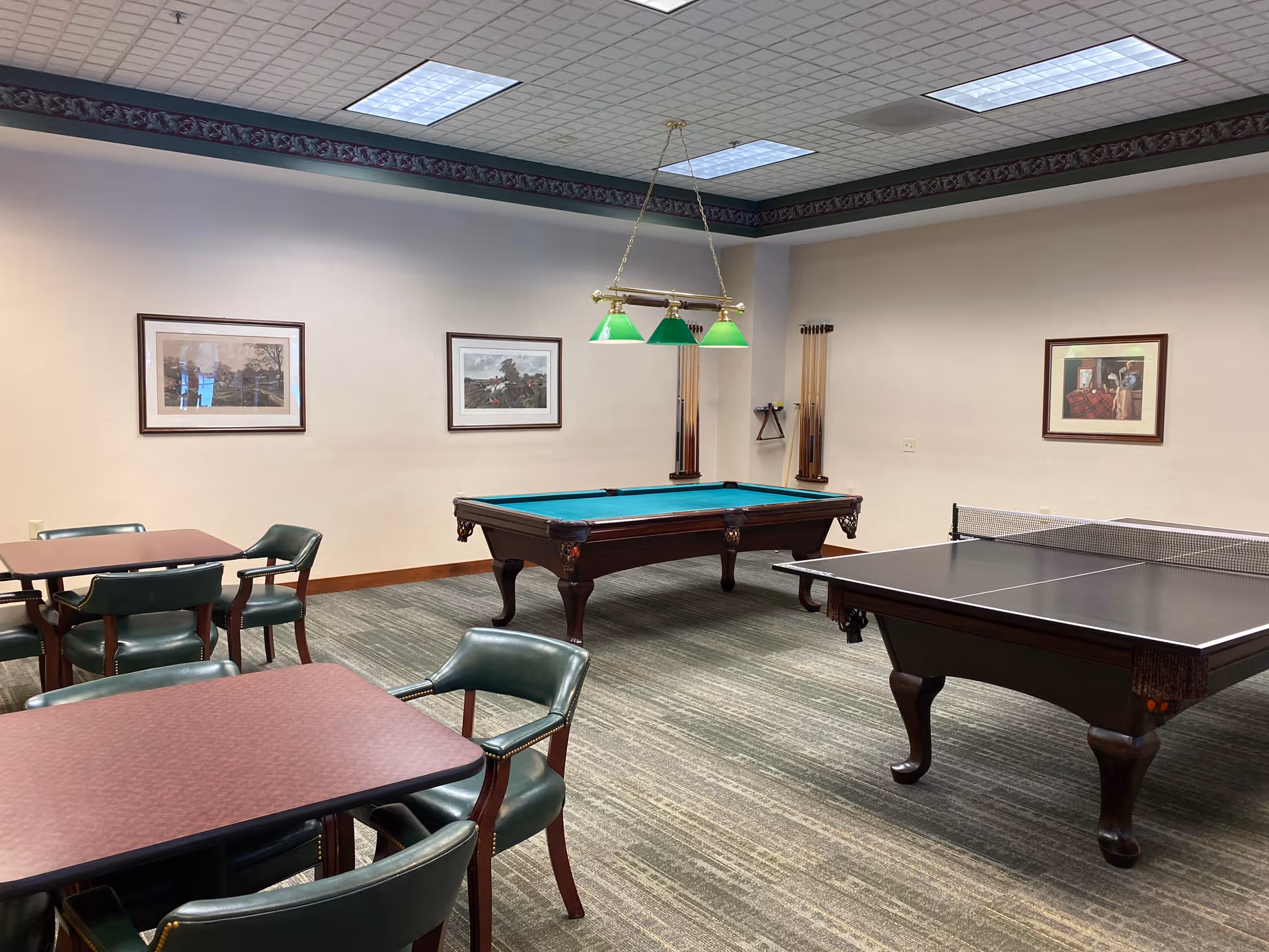 Game room with a pool table, ping-pong table, and several card tables and chairs under fluorescent lighting.