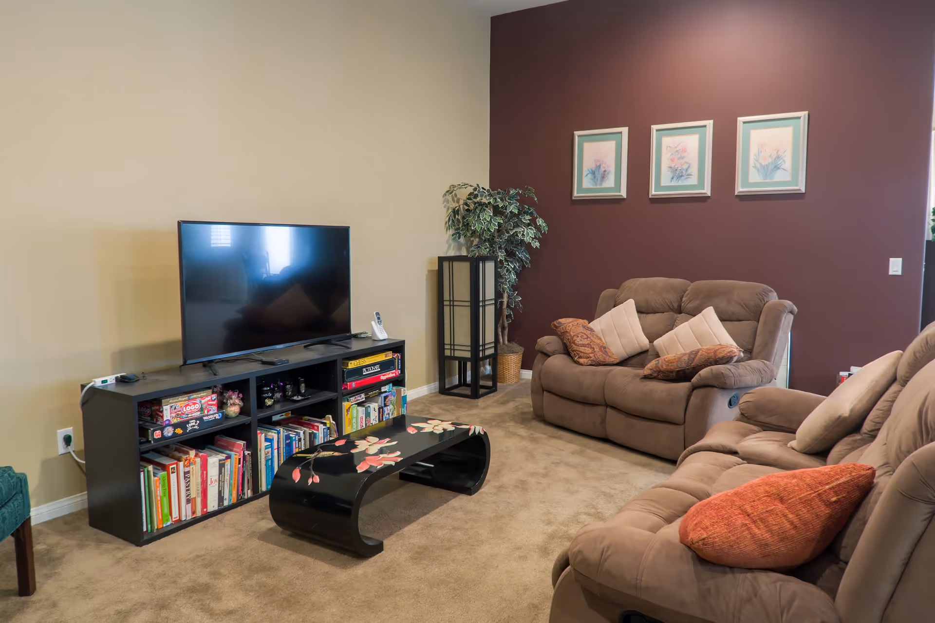 Cozy living room with reclining sofas, a TV on a media console, a decorative coffee table, and framed artwork on a painted accent wall.