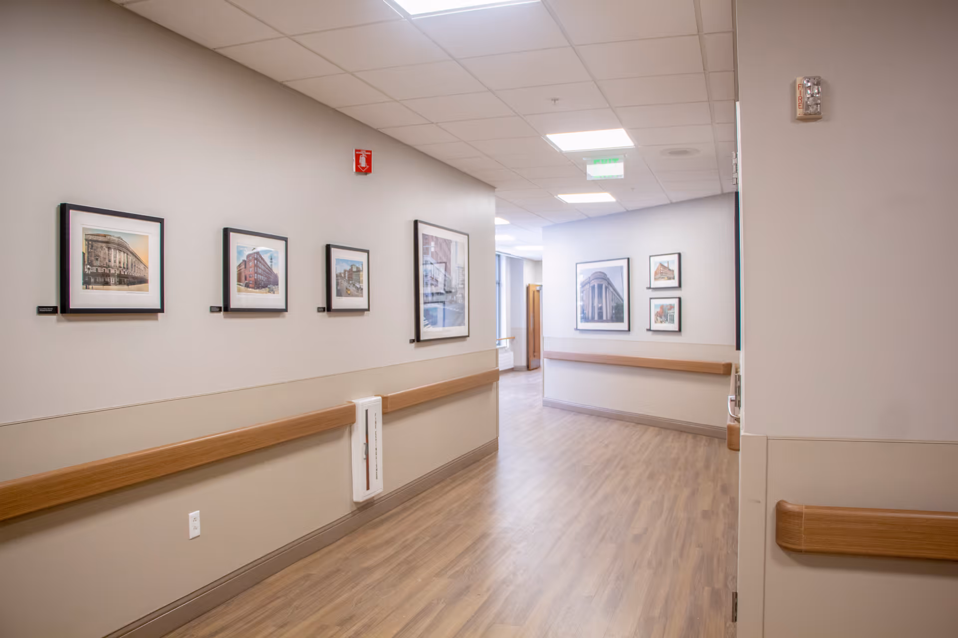 Well-lit interior hallway with framed artwork, wooden handrails, and wood-look flooring.