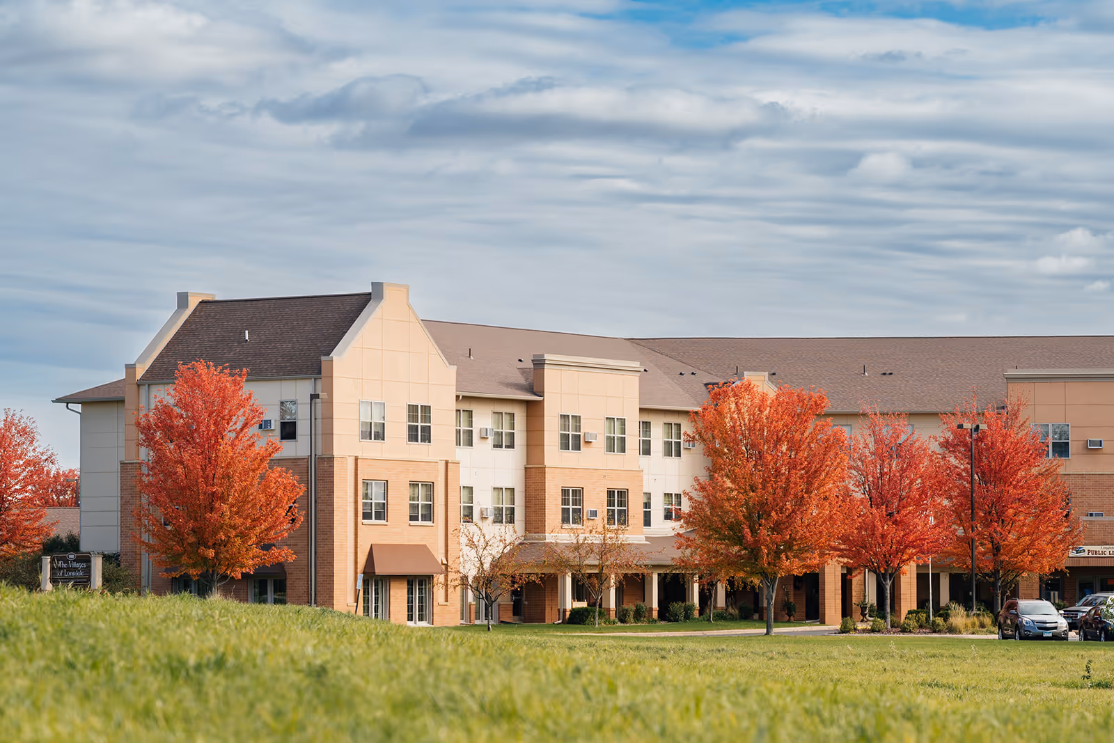 Three-story residential building with fall-colored trees and a grassy lawn in front.