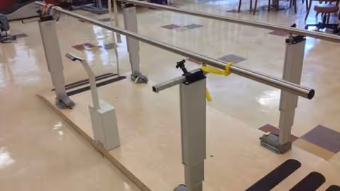 Rehabilitation gait training parallel bars in a bright interior hallway of a senior living facility.