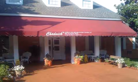 Front entrance of Chadwick Nursing & Rehab Center with a red awning and potted plants.
