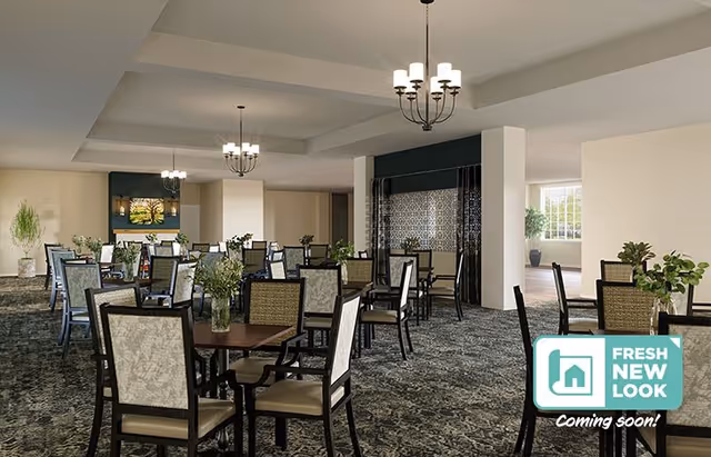Spacious dining room with multiple tables and chairs, chandeliers, carpeted floor, and plants, with a 'Fresh New Look Coming soon!' badge in the corner.