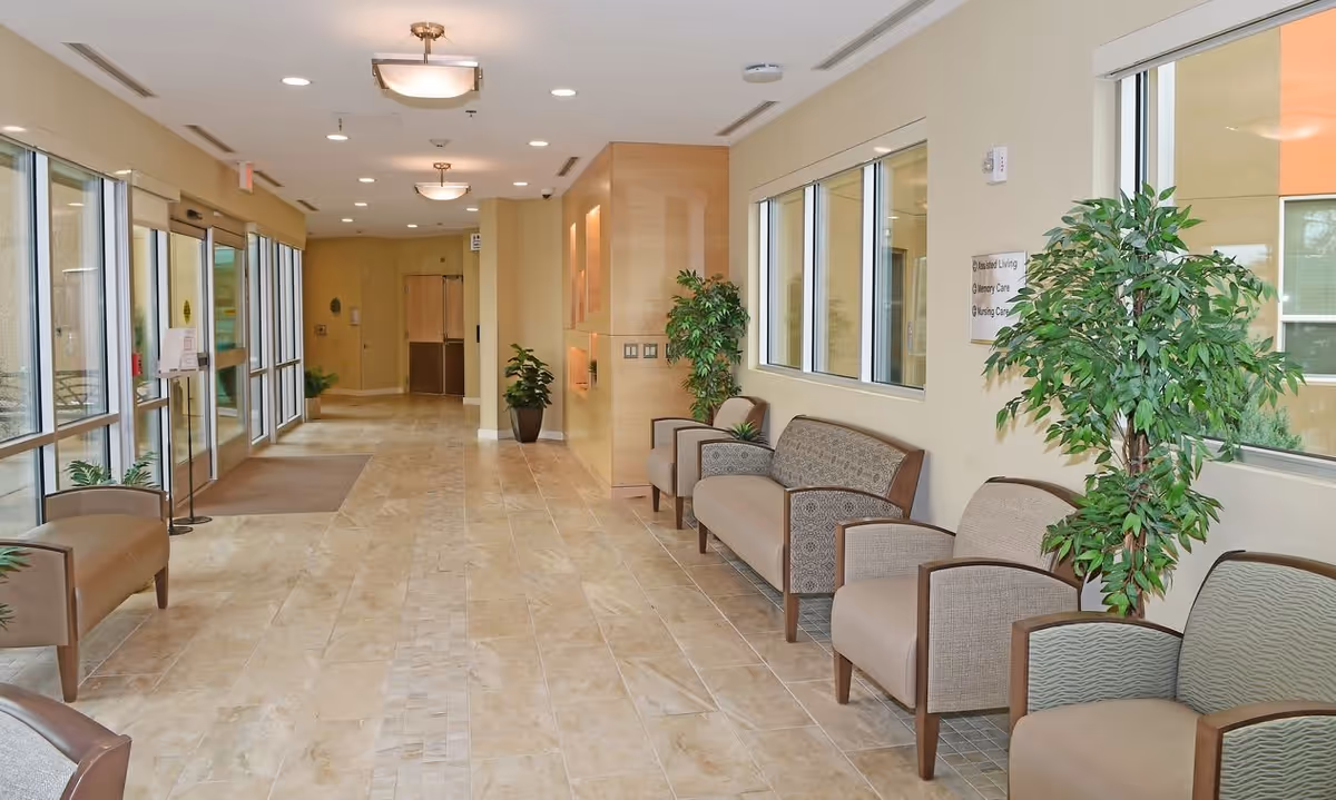 Spacious, well-lit lobby with tiled floors, rows of chairs, potted plants, and large windows.