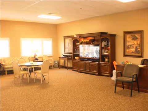 Spacious senior living common area with round table, chairs, and a large TV cabinet.