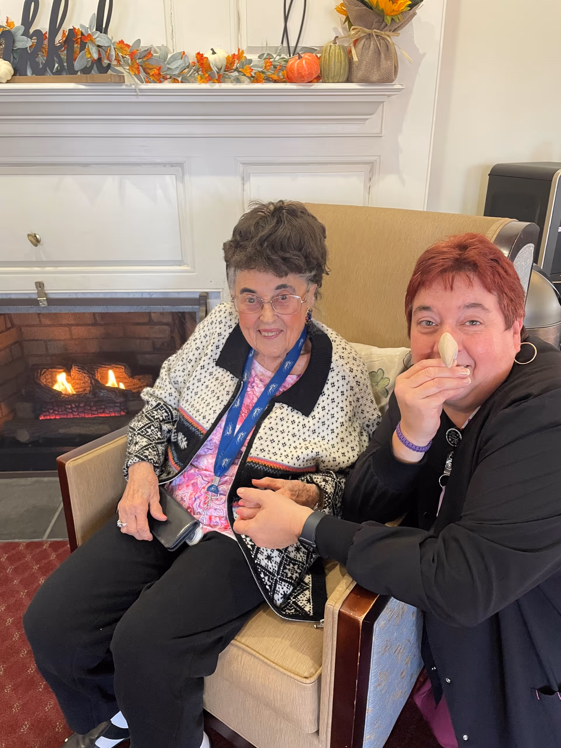 Two people sitting in armchairs beside a lit fireplace in a decorated lounge area.