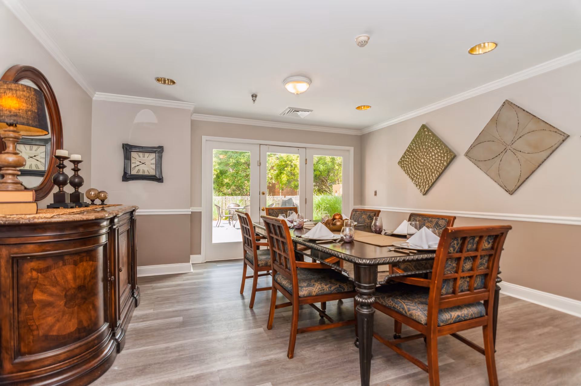 Bright dining room with a set wooden table and chairs, sideboard, wall art and glass doors opening to a patio.