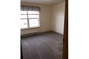 Empty carpeted bedroom with a window, valance, and baseboard heater.