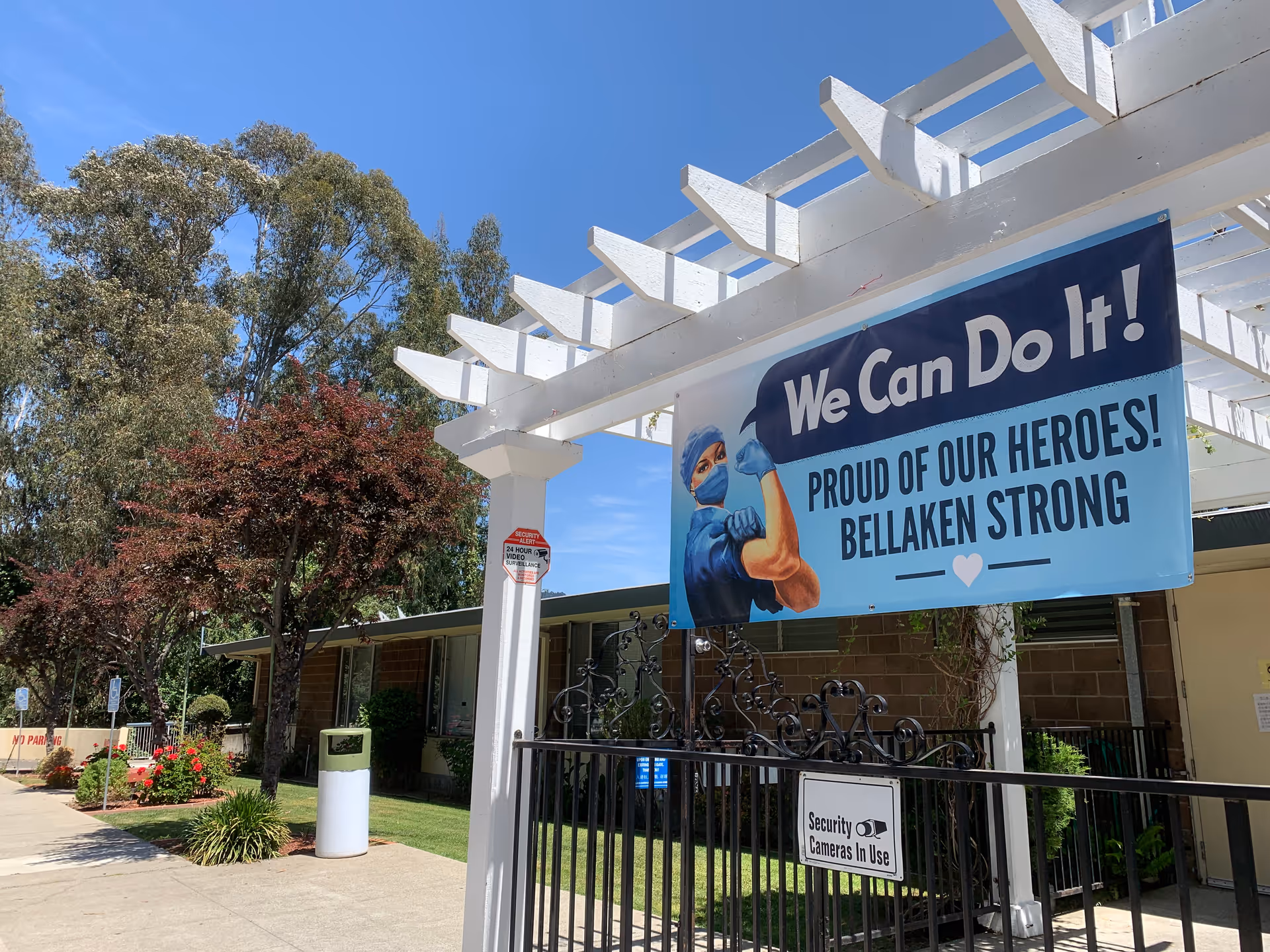 Front entrance of Bellaken Garden showing a pergola and gated walkway with a large 'We Can Do It! Proud of Our Heroes! Bellaken Strong' banner.