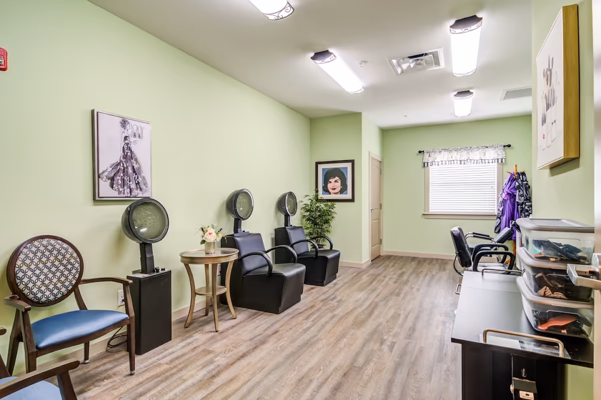 Interior salon room with seated hair dryers, chairs, styling stations, and light green walls.