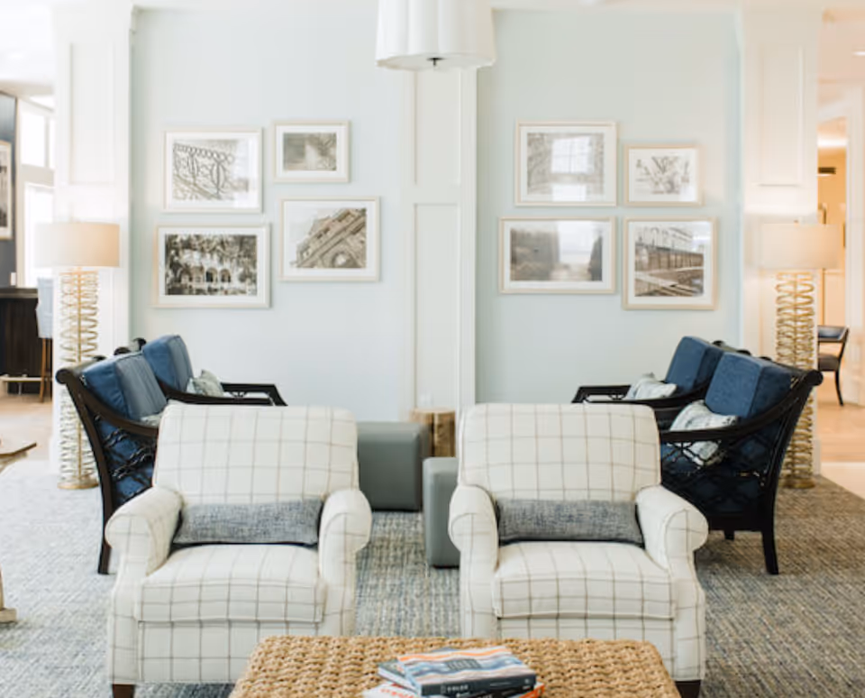 Bright seating area with two plaid armchairs, blue sofas, framed wall art, and floor lamps in a lounge.
