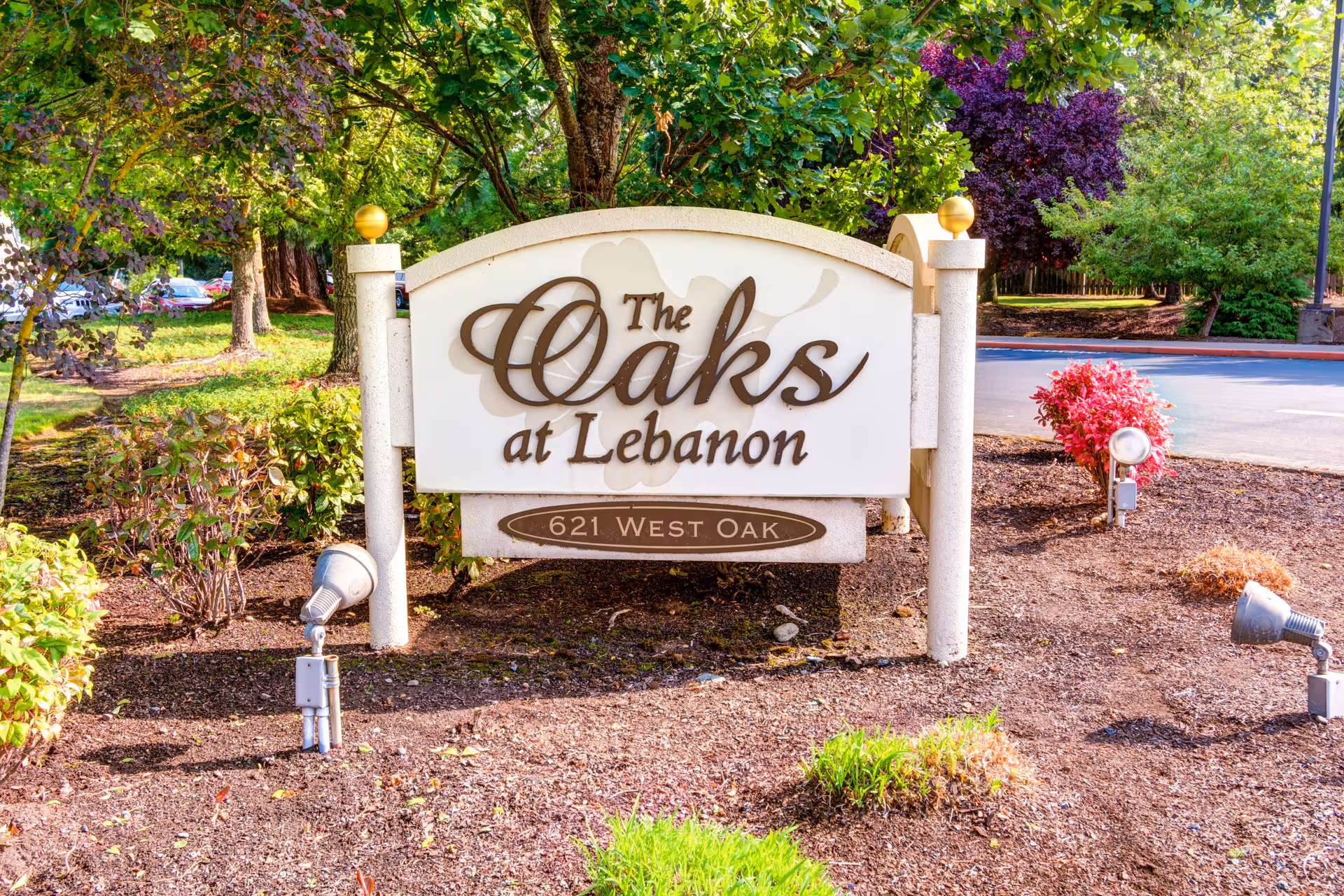 A large outdoor sign for The Oaks at Lebanon, located at 621 West Oak, surrounded by landscaped plants and trees with a paved road in the background.