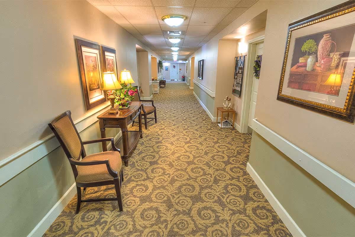 Well-lit decorated interior hallway with chairs, a side table and lamps, patterned carpet, and framed artwork.